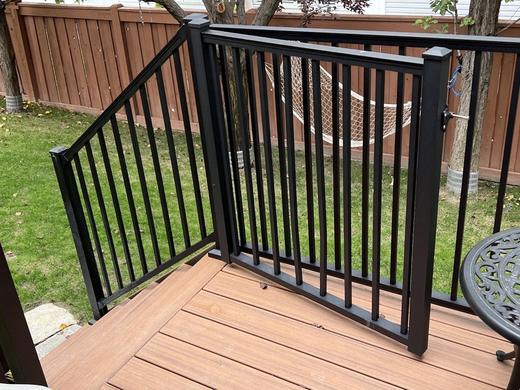 Black metal picket railing with self-closing gate on brown composite deck above stairs (Trex Signature)