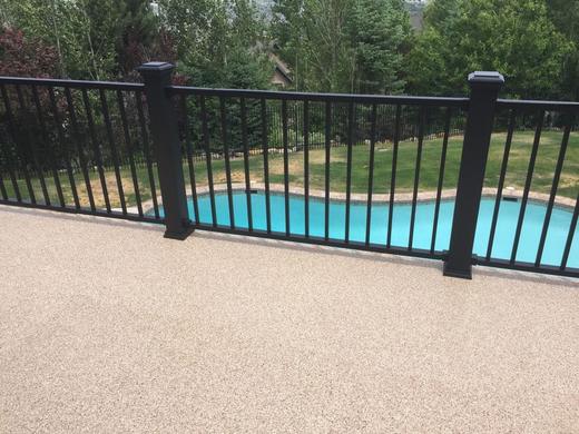 Black metal picket railing on textured deck surface overlooking backyard pool and lawn (Trex Transcend)