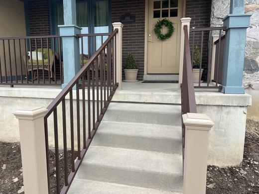 Brown metal picket railing with white post sleeves along concrete steps to covered porch (Trex Transcend in Rope Swing)