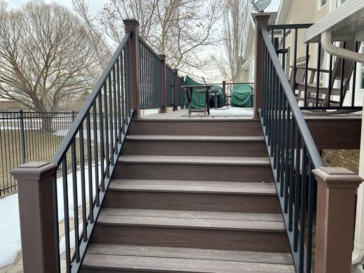 Wide composite stairs with black metal pickets and brown post sleeves leading to deck (Trex Transcend)