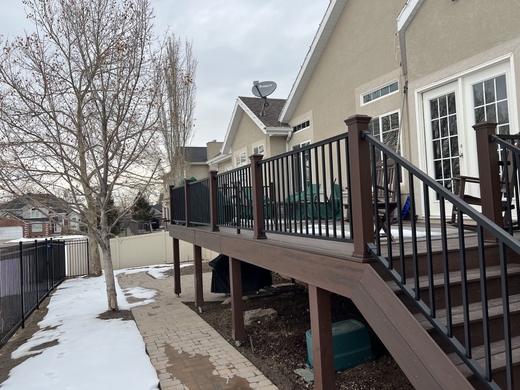 Raised deck with black metal pickets and brown composite rails and stairs in winter yard (Trex Transcend)