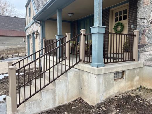 Bronze metal picket railing along stone porch steps under a covered front entry (Trex Signature)
