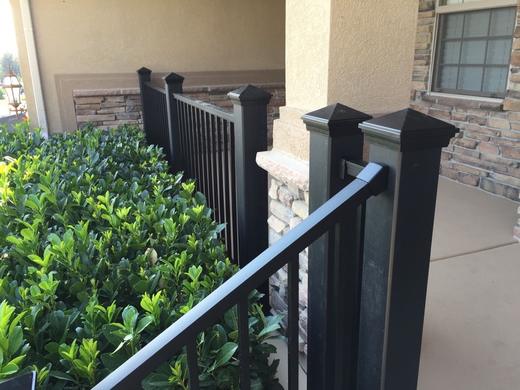 Black metal railing with vertical pickets and capped posts beside stone-faced covered entry (Trex Transcend)