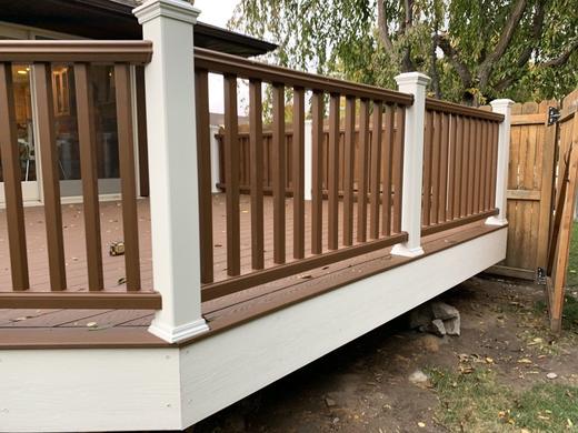 Brown composite deck railing with vertical pickets and white post sleeves beside wood fence (Trex Transcend in Tree House)