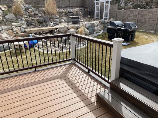 Brown composite deck with black metal pickets, brown top rail and white post sleeve (Trex Transcend in Vintage Lantern)