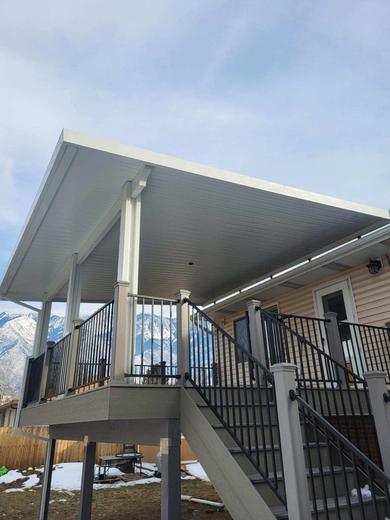 Covered deck with white posts, black metal balusters, stairs and snowy mountain backdrop (Trex Transcend in Gravel Path)
