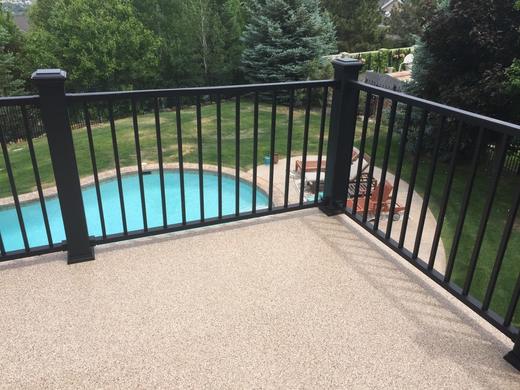 Black aluminum picket railing on textured deck surface overlooking backyard pool and lawn (Trex Transcend)