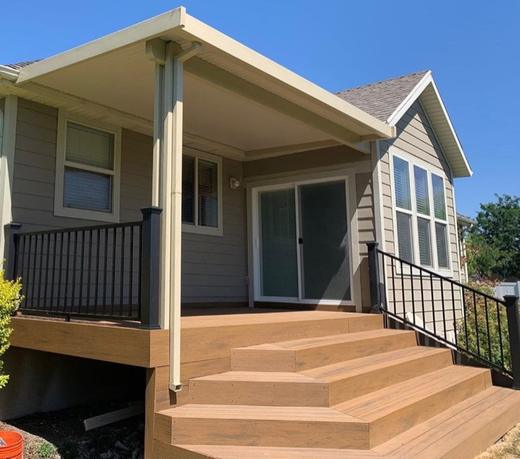 Covered deck with brown composite decking, black metal picket railing and wide stairs (Trex Transcend)