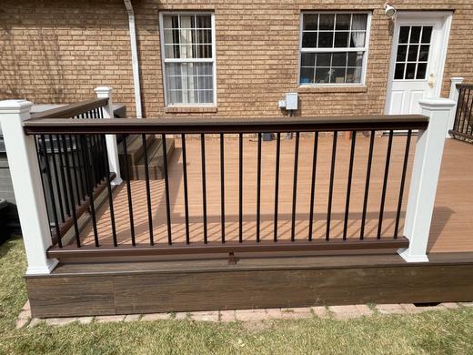 Brown composite railing with black metal balusters and white posts beside brick home (Trex Transcend)