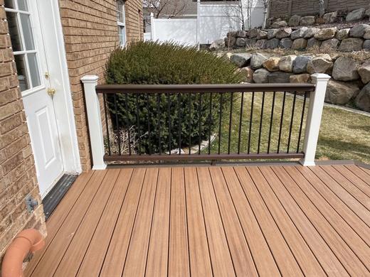 Low deck with brown composite boards, black balusters, white posts beside brick house (Trex Transcend)