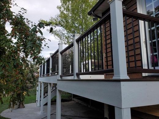 Raised deck with black metal balusters, brown top rail and white post sleeves (Trex Transcend in Vintage Lantern)
