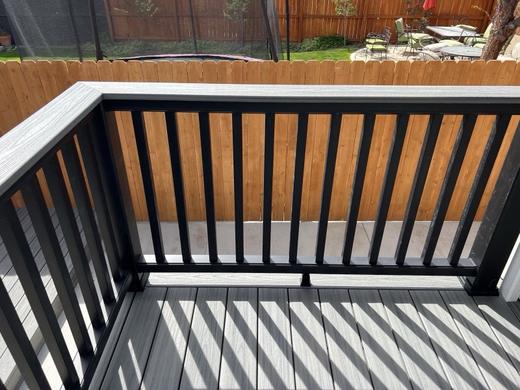 Black metal picket railing with gray composite top rail on gray deck by wood fence (Trex Transcend)