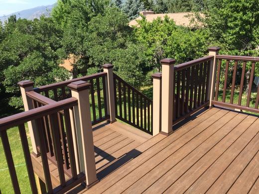 Composite deck with brown rails, tan posts and black metal balusters overlooking trees (Trex Transcend in Tiki Torch)