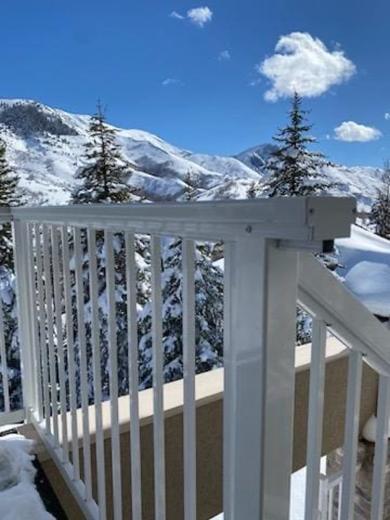 White vertical picket railing on snowy balcony overlooking pine-covered mountains under blue sky