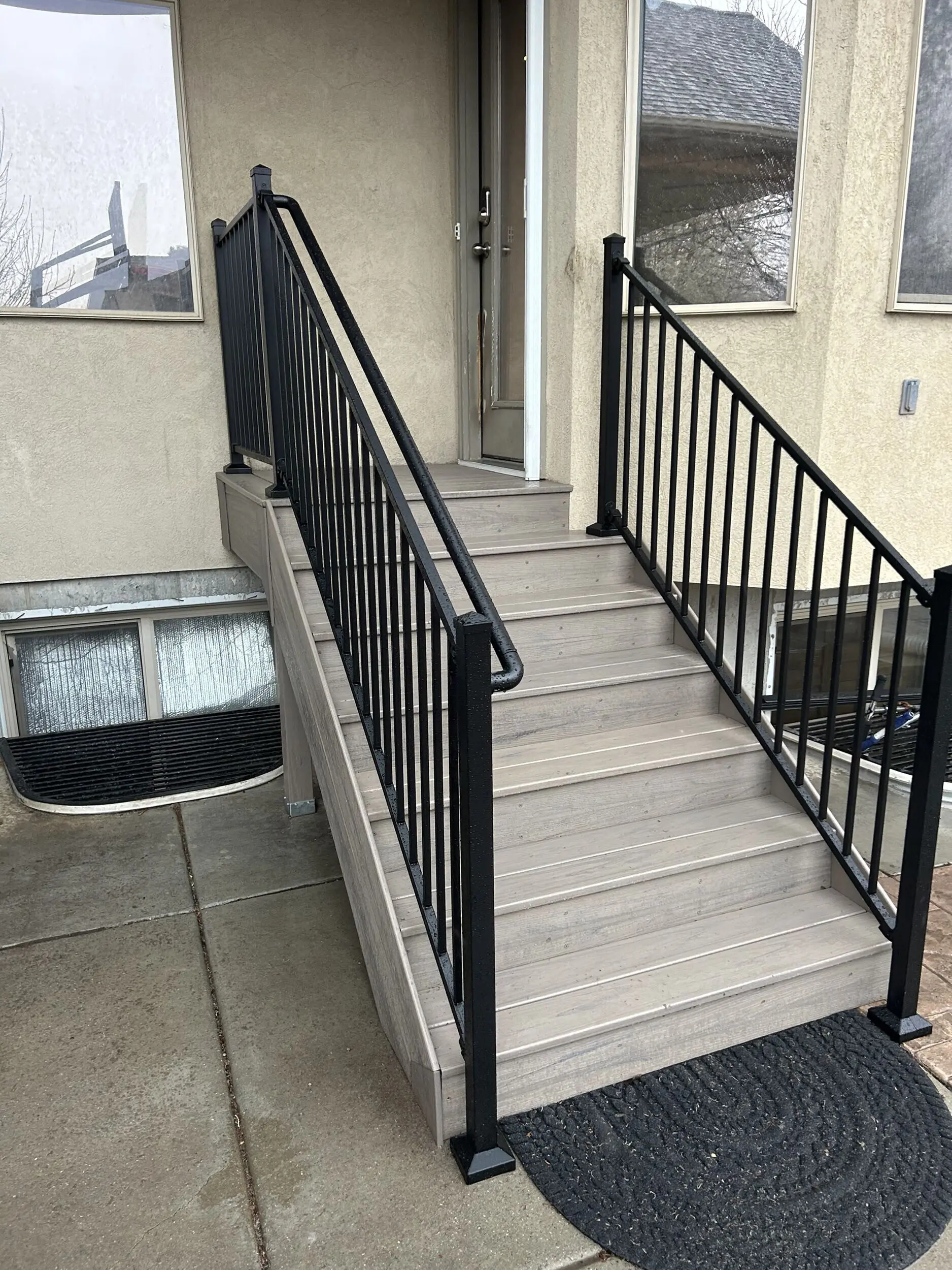 IMG_4236 A set of concrete steps with a black metal railing leading up to a covered porch or entryway of a residential building.