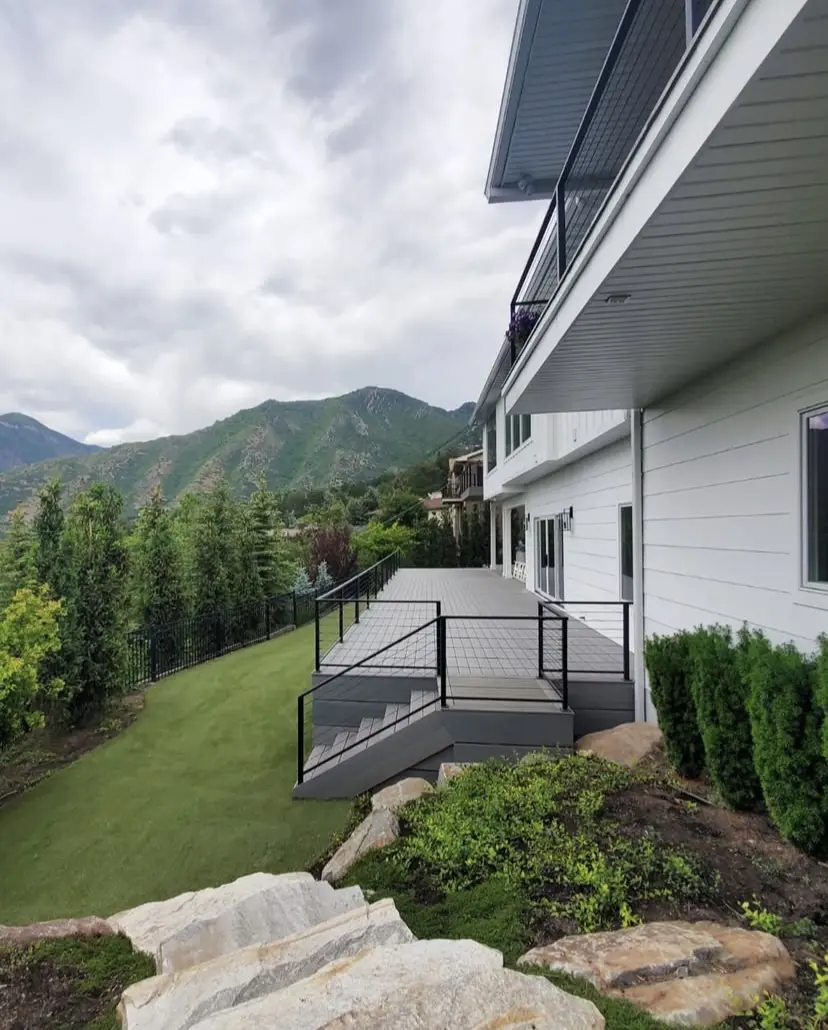 A deck with a metal railing overlooking a mountainous, forested landscape.
