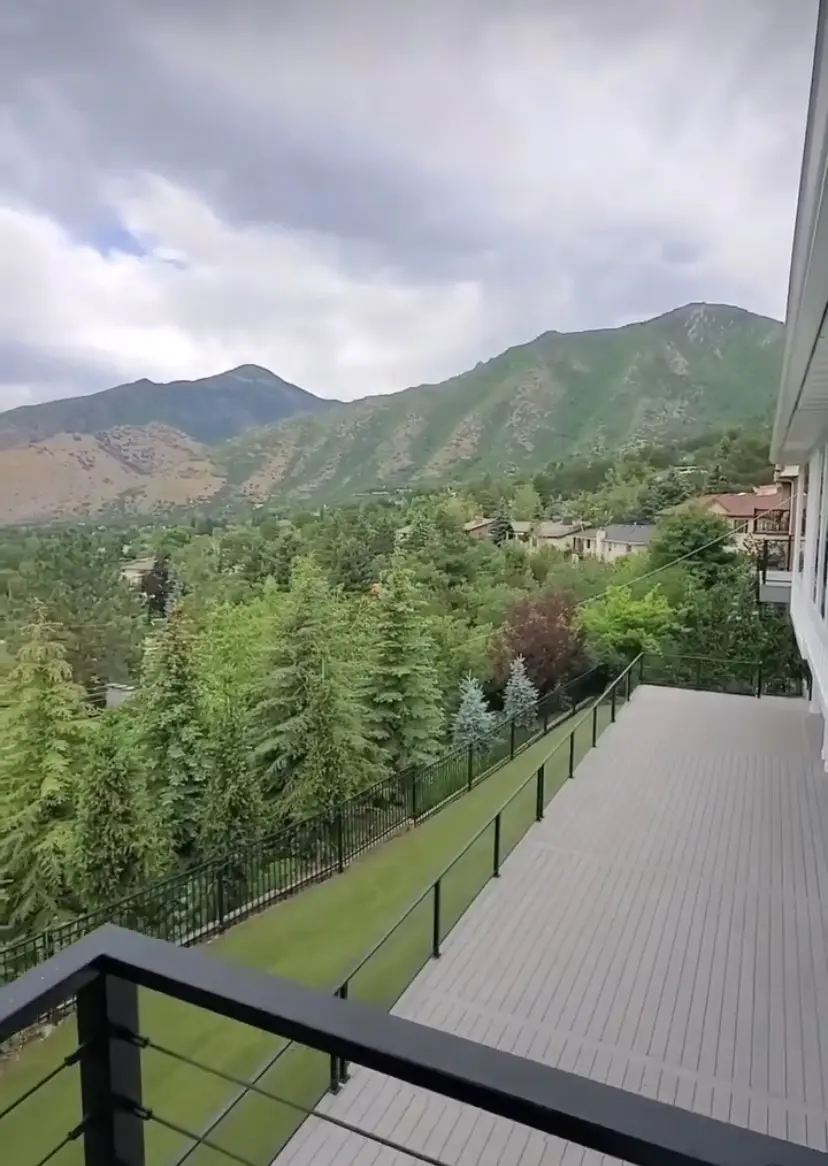 A scenic view of mountainous terrain with a white building and a balcony in the foreground, surrounded by lush greenery.