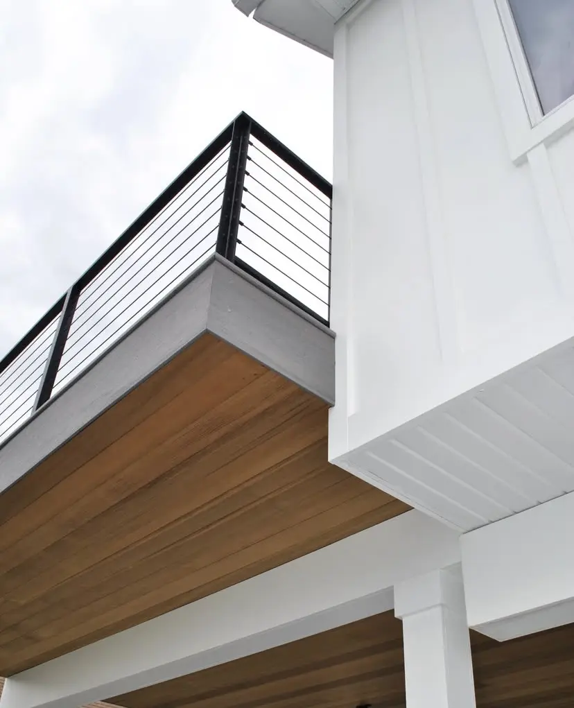 A close-up view of the roof overhang and balcony of the house, showcasing the angular, modern design with exposed wooden beams and black metal railings.