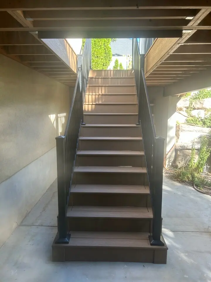 A set of stairs leading up to a raised wooden deck or patio, with a pergola overhead and a view of the surrounding landscaping