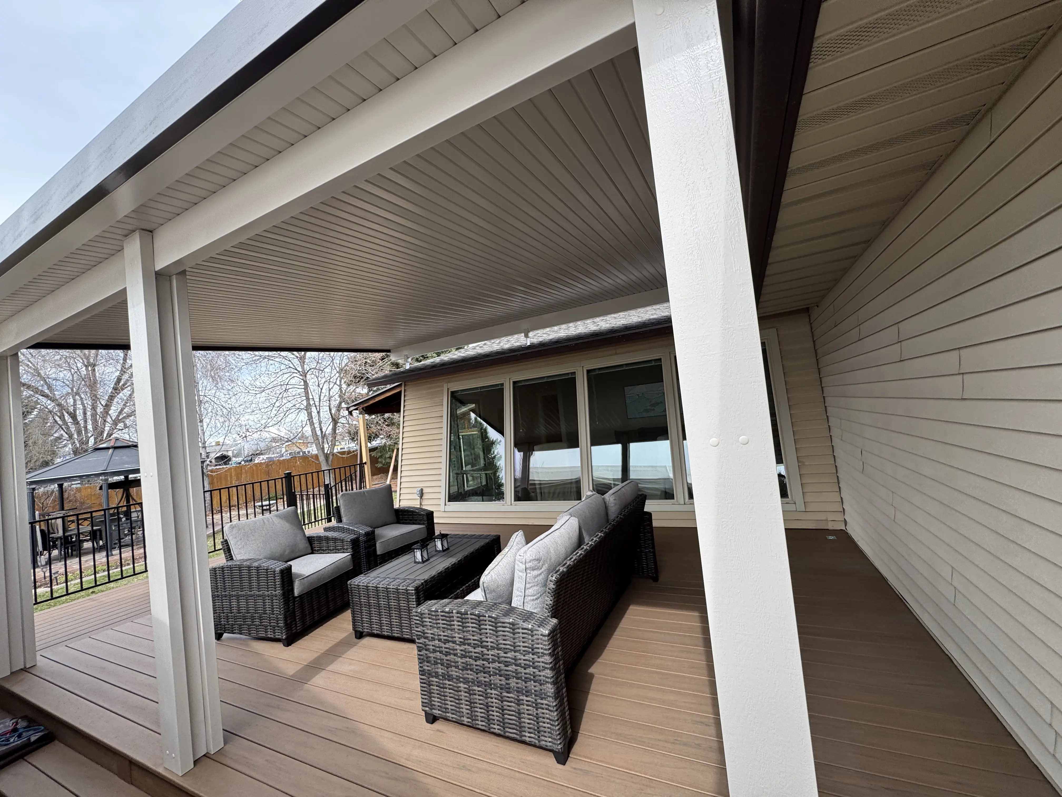 A close-up view of the covered porch with grey wicker furniture and a tiled ceiling.