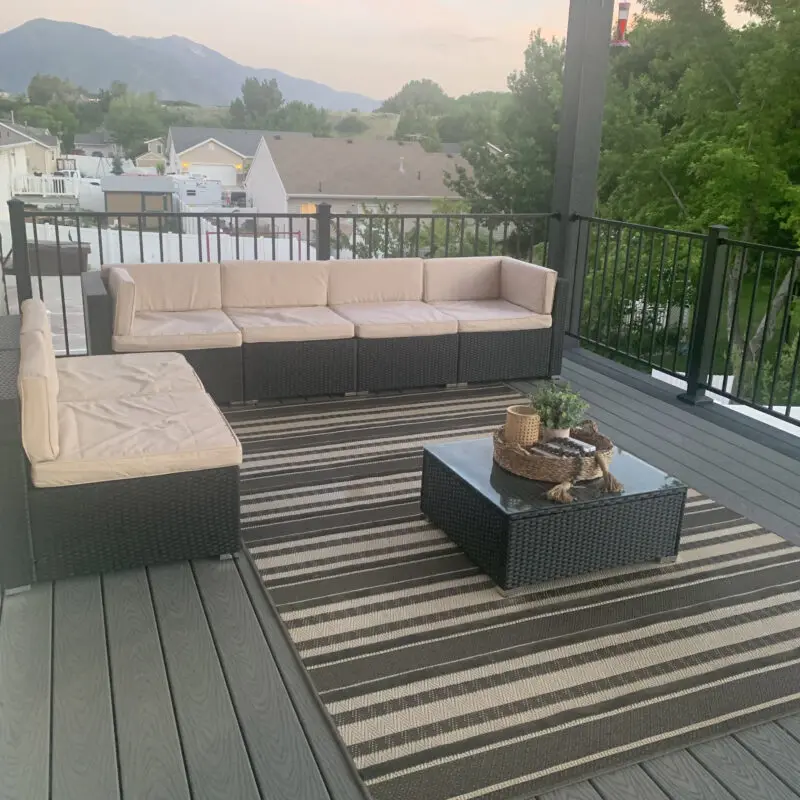 A patio with a sectional sofa, coffee table, and striped rug, with a mountain view in the distance.
