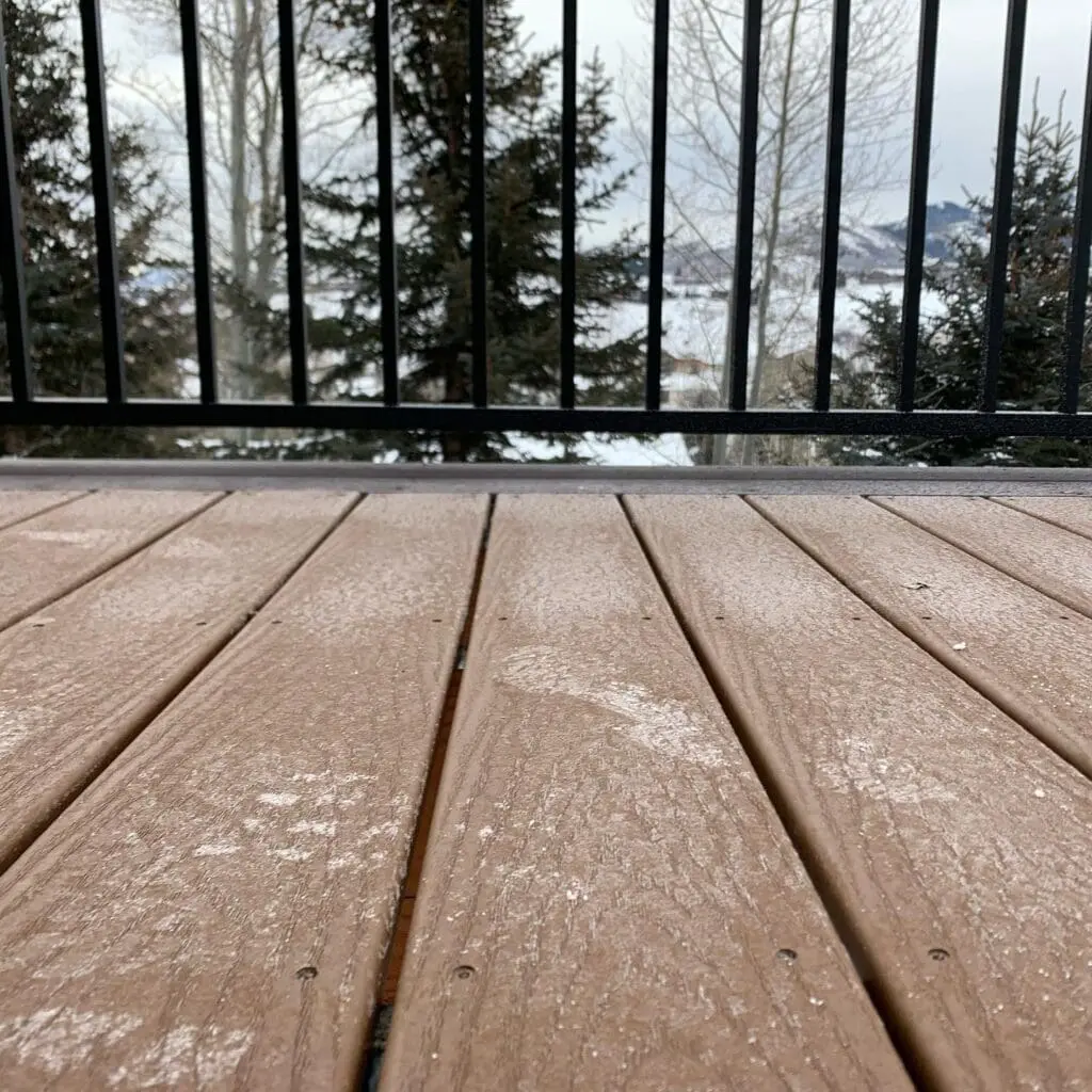 composite deck with snow on it overlooking a wooded area