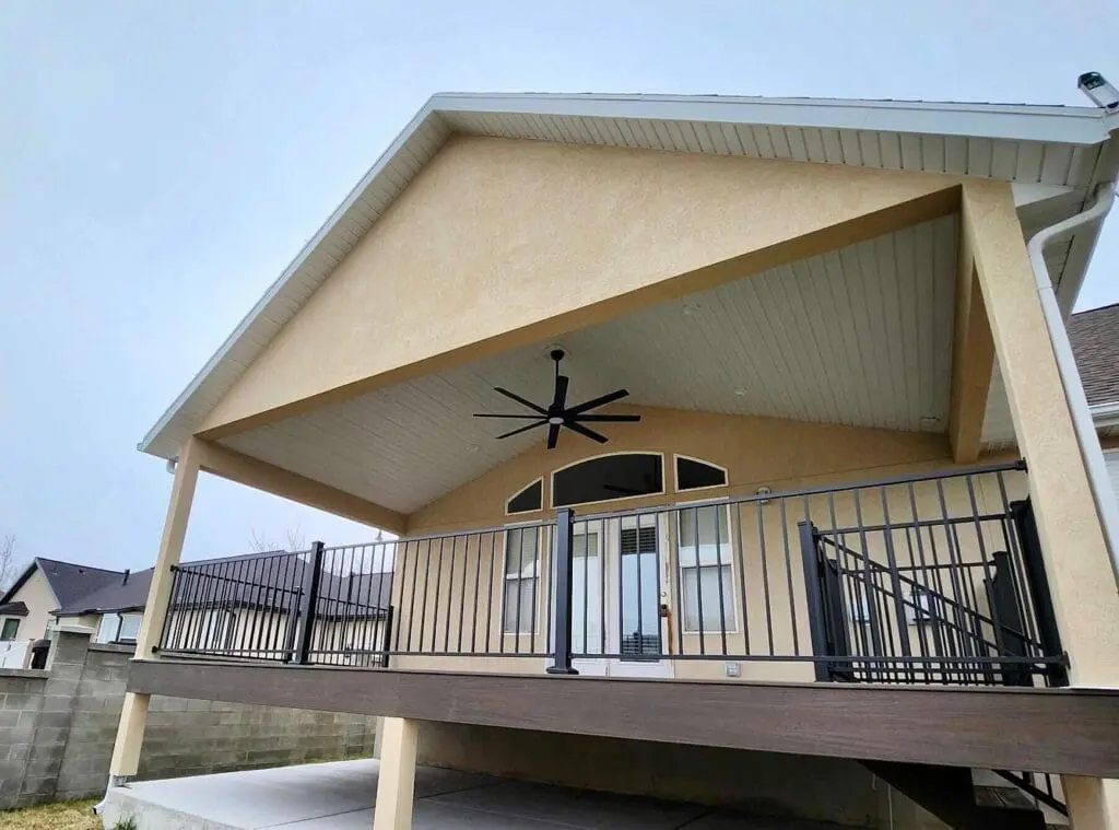 A raised deck featuring a custom deck roof that matches the existing roof on the home. The roof has a fan, lighting and covers the entire deck. The deck is made of composite wood and has a railing for safety.