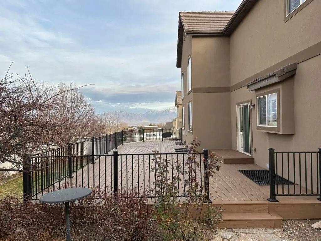 a composite deck on the first floor of a home.  It runs the full length of the home and has a railing around it for safety. 