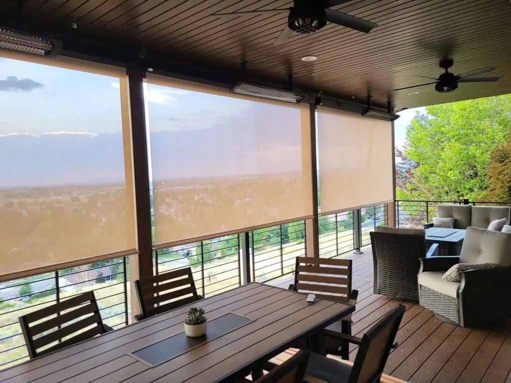 second story composite deck in brown tones with a vertical steel railing and mesh sun shades. custom deck roof with lights, heat and fans.