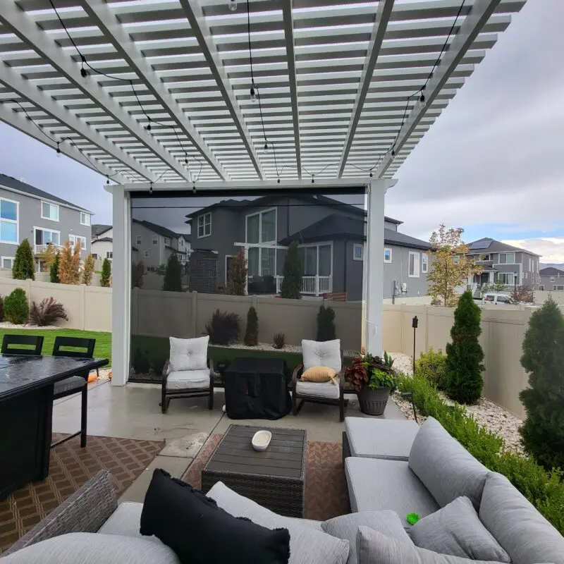 backyard patio space with a white pergola and a drop down sun shade.
