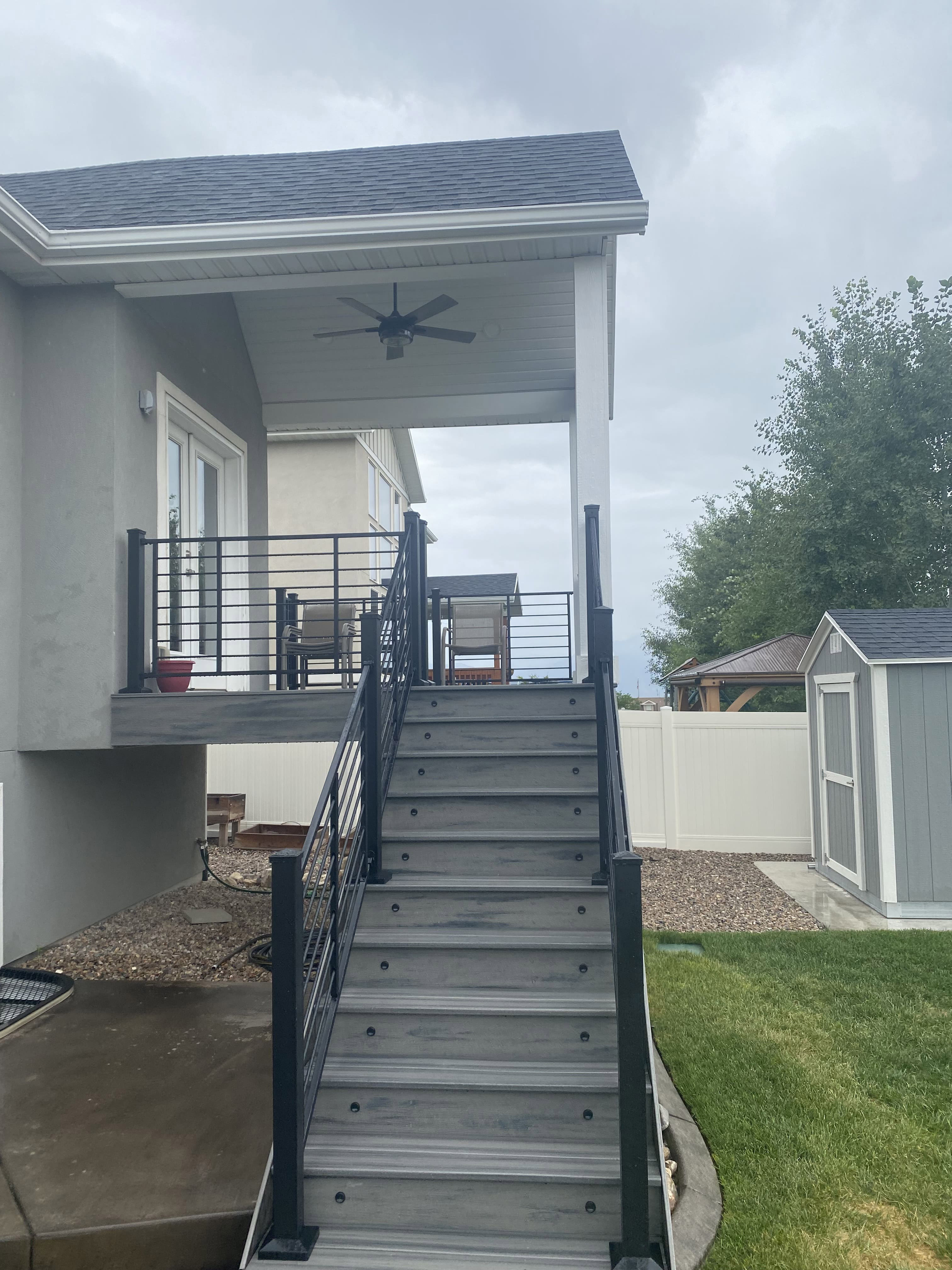 Custom-Vaulted-Roof-1-2 A white house with a covered porch and a metal staircase leading up to it. The yard has grass and some landscaping.