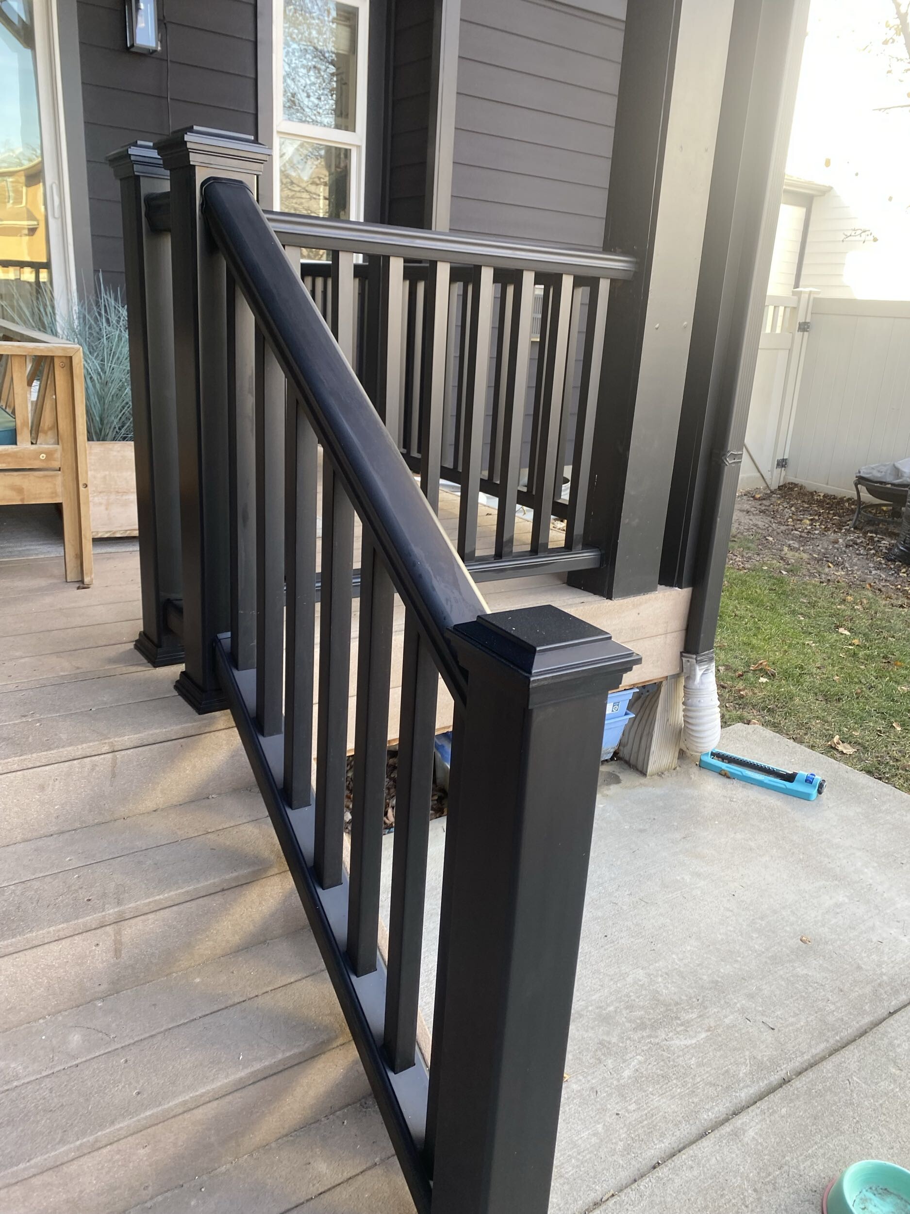A close-up view of a black railing on a wooden deck, with landscaping elements visible in the background.