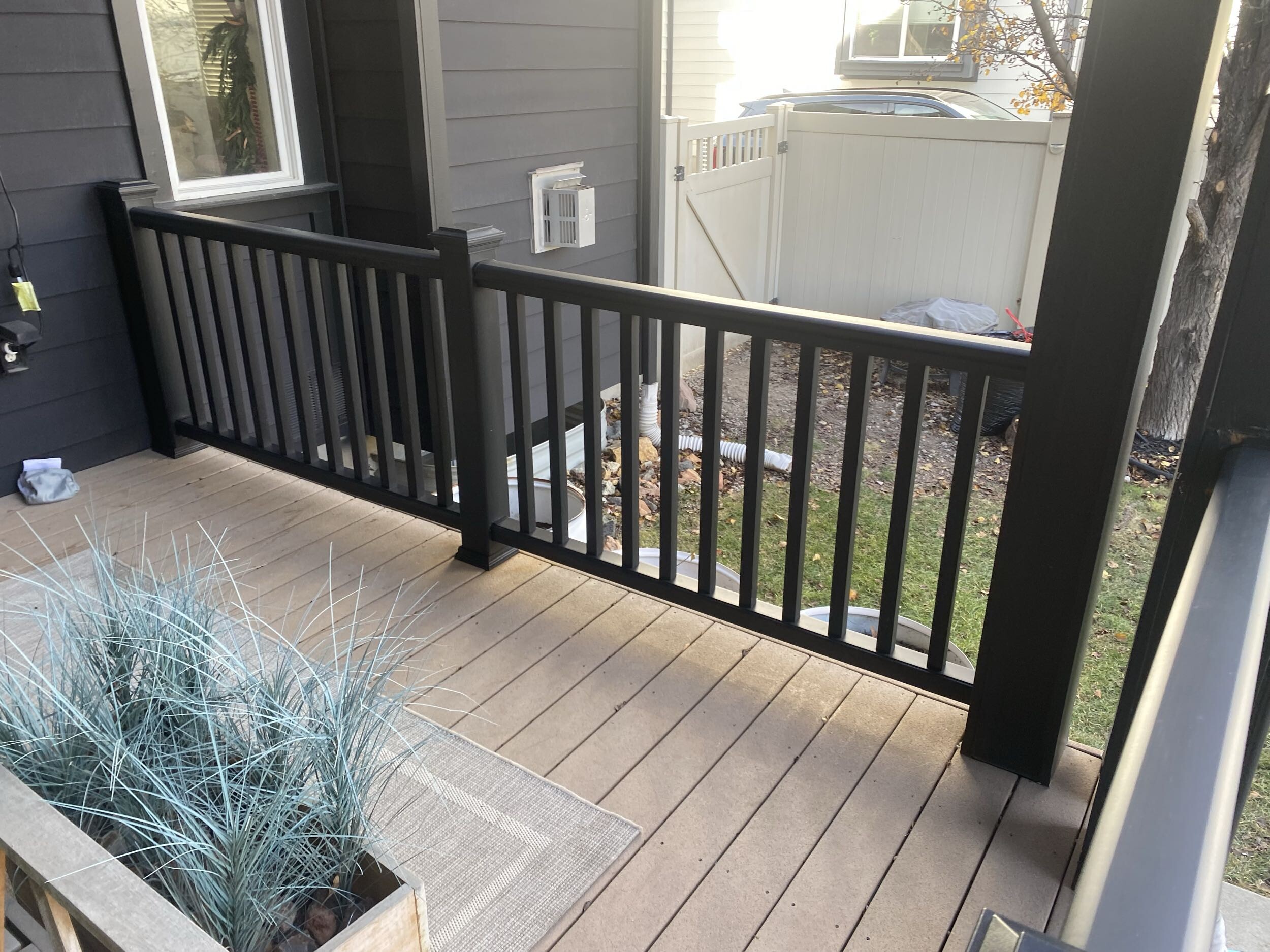 A wooden deck with a black railing, surrounded by a wooden fence and landscaping features.