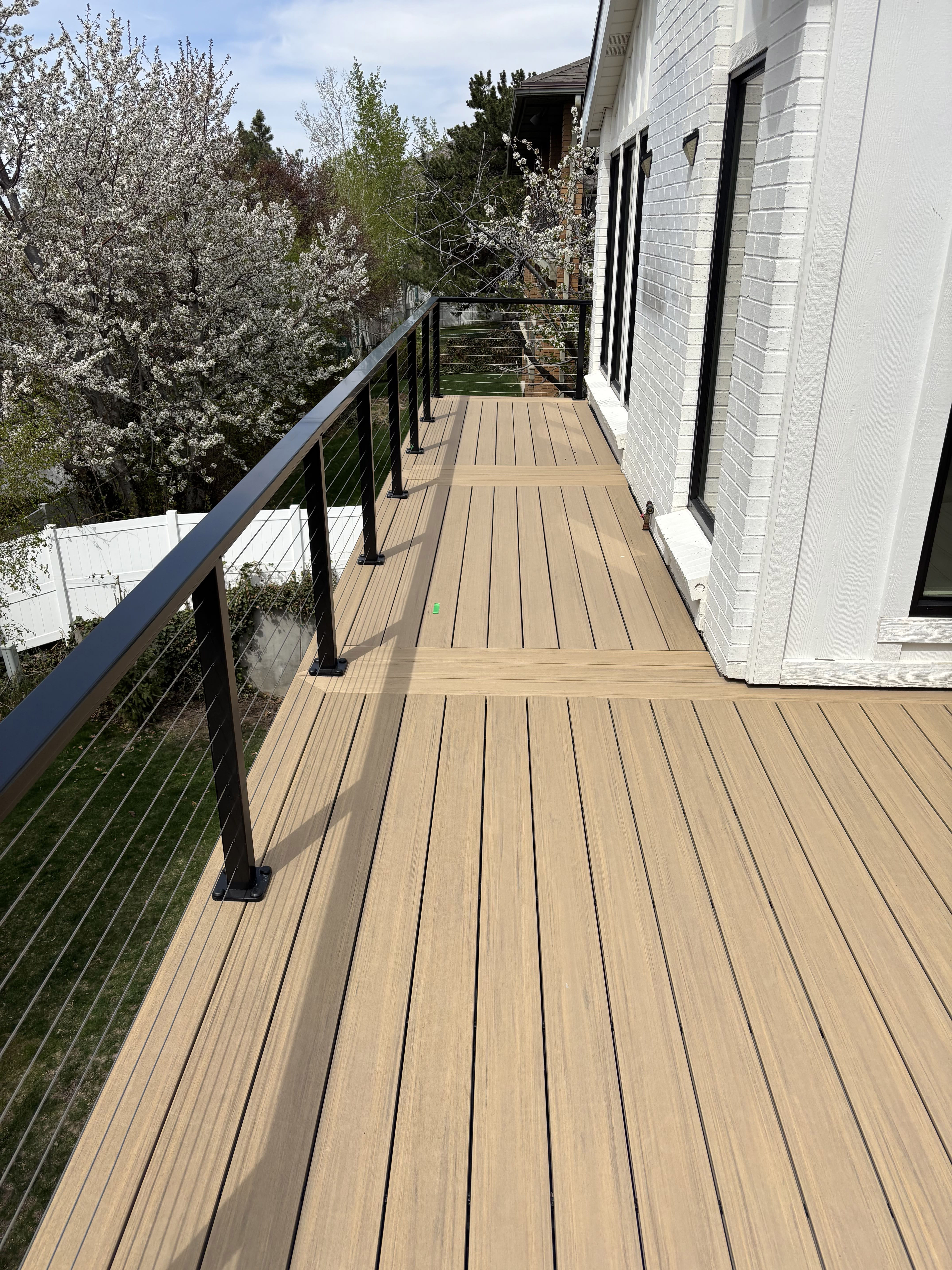 A wooden deck with a metal railing overlooking a forested area. The deck appears to be attached to a residential building.