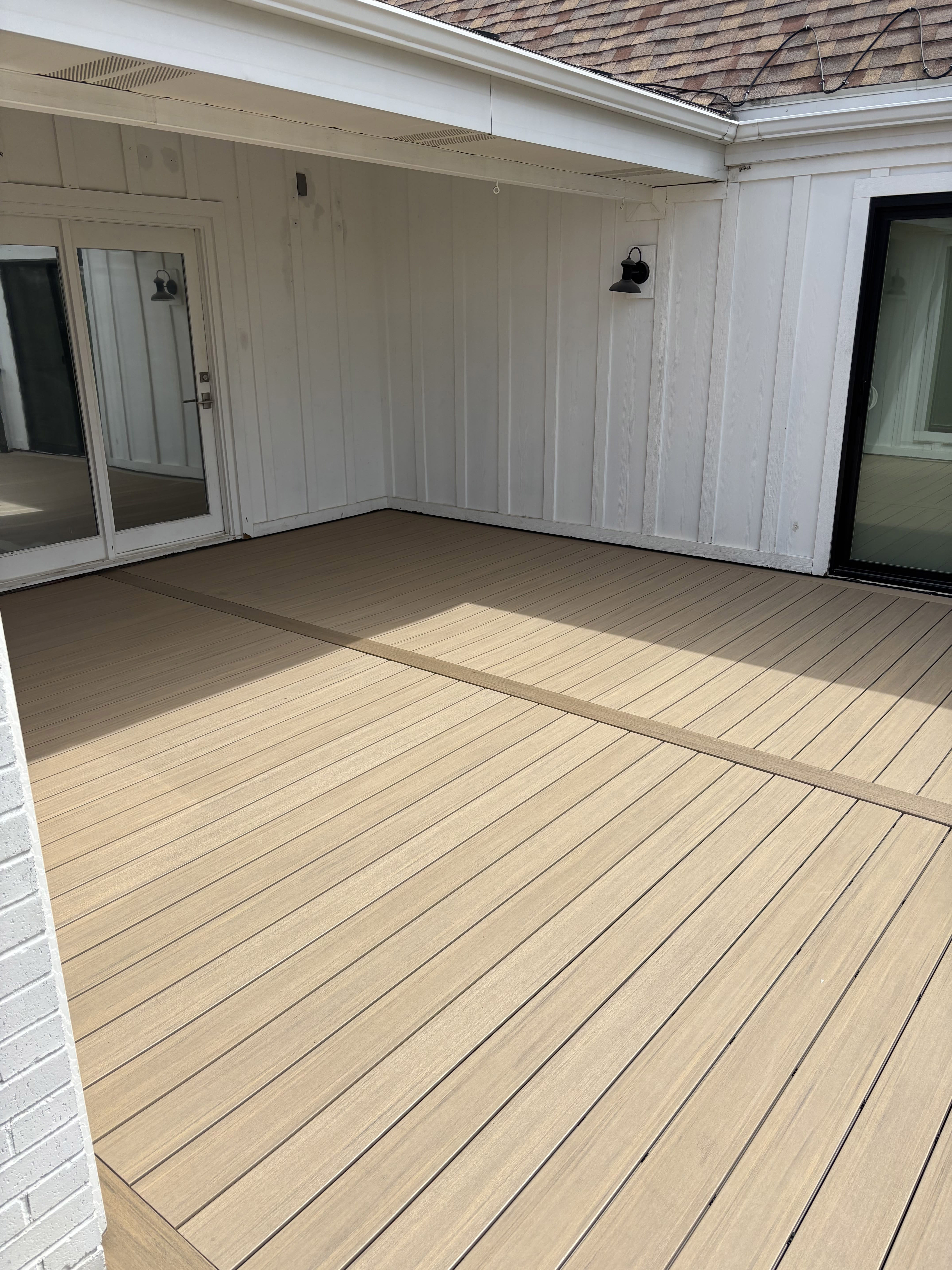 A covered outdoor deck with a wooden floor and white paneled walls, featuring a sliding glass door and an empty space ready for furnishing.
