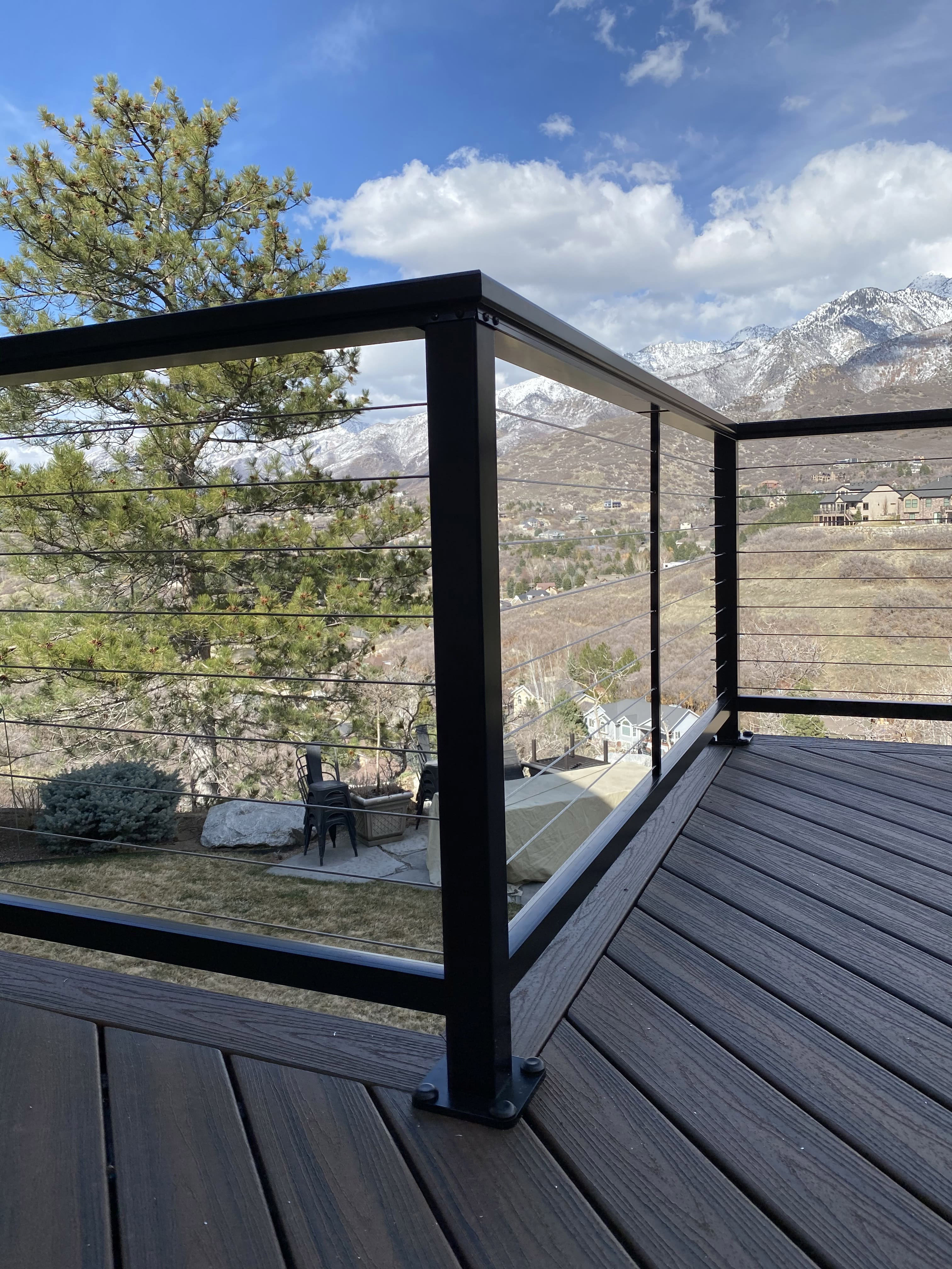 A wooden deck with a metal railing overlooking a snowy mountain landscape. The deck has a clear glass railing, allowing for an unobstructed view of the mountains.