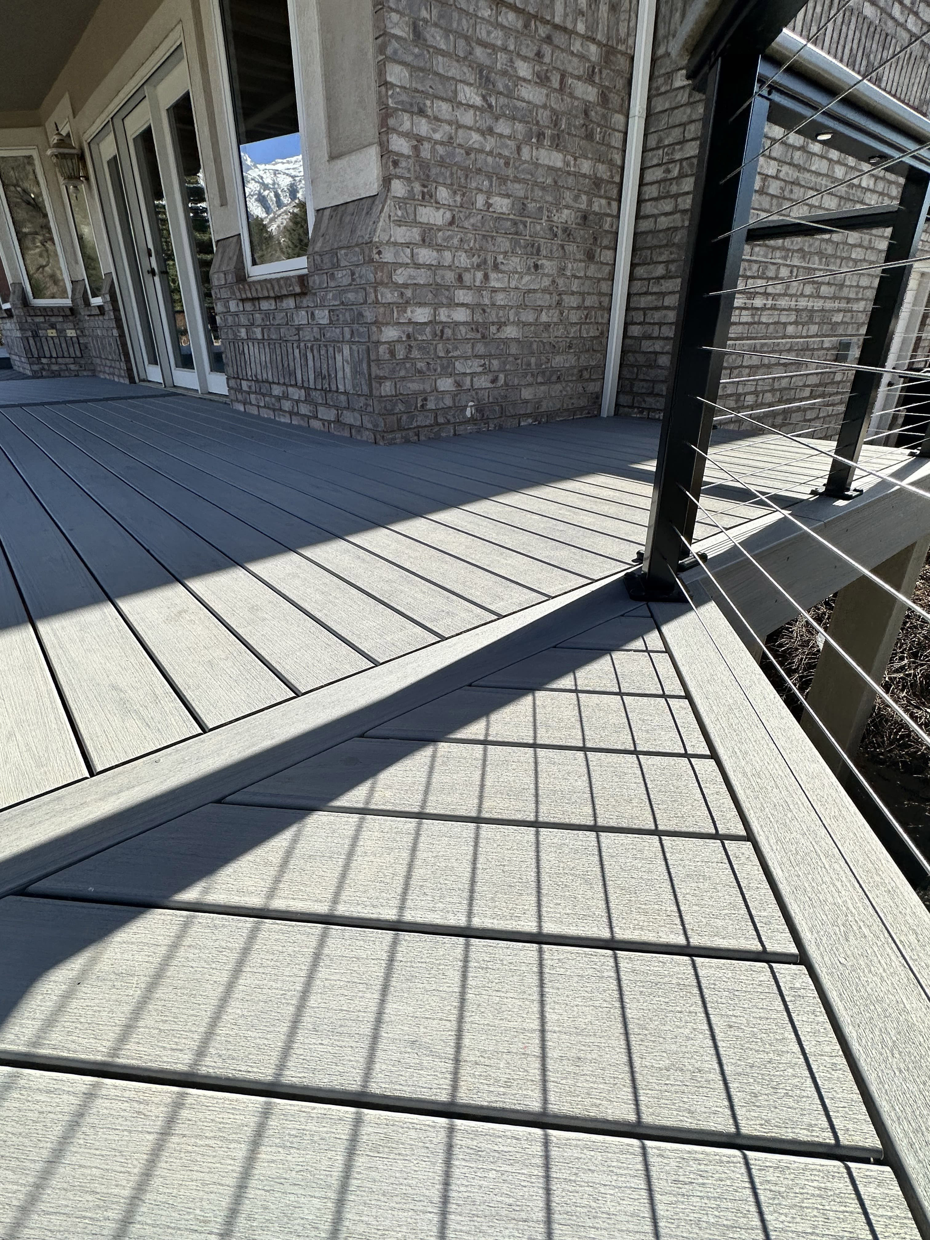 Trex-Lineage-Rainier-Decking-1-27 A wooden deck with a metal railing and a decorative pattern on the floor, overlooking a snowy landscape.