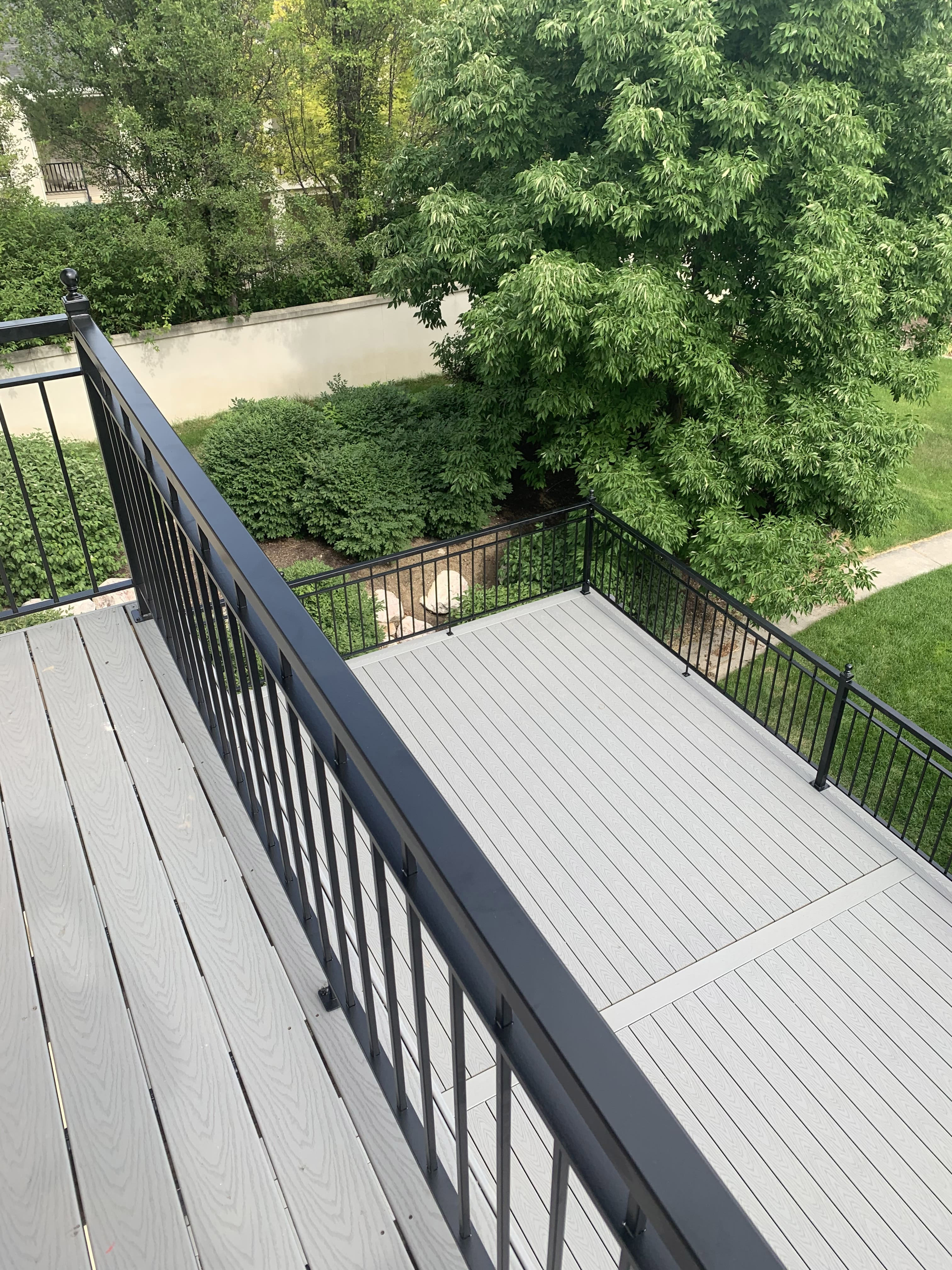 Trex-Select-Pebble-Grey-10-45 A gray wooden deck with a railing overlooking a wooded backyard area.