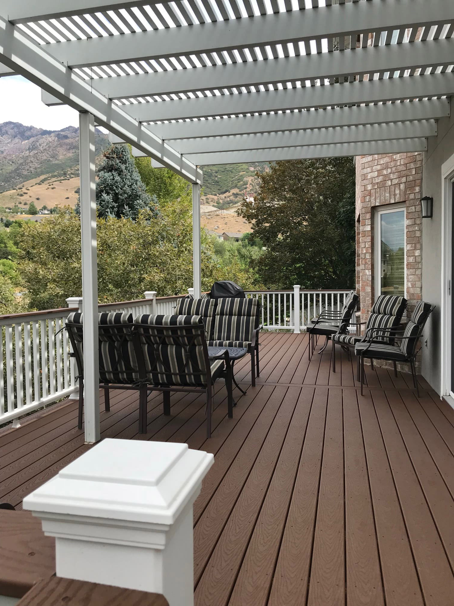 Trex-Select-Saddle-8-60 A covered patio with a gray metal awning and striped cushions on the outdoor furniture. The patio overlooks a mountainous landscape.