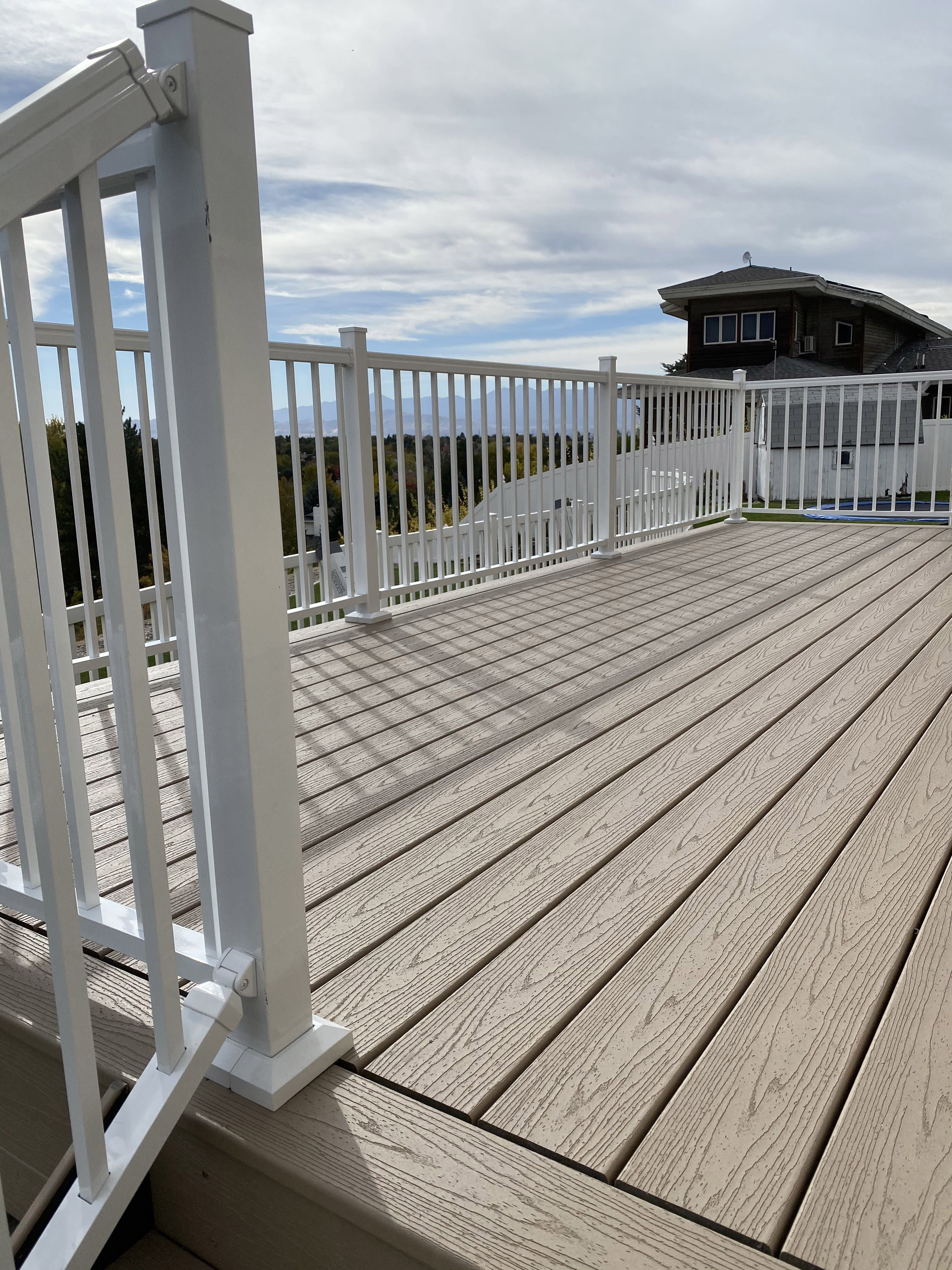 Trex-Transcend-Rope-Swing-25 A wide gray wood deck with a white railing, extending out from a house with a porch roof and surrounded by trees.