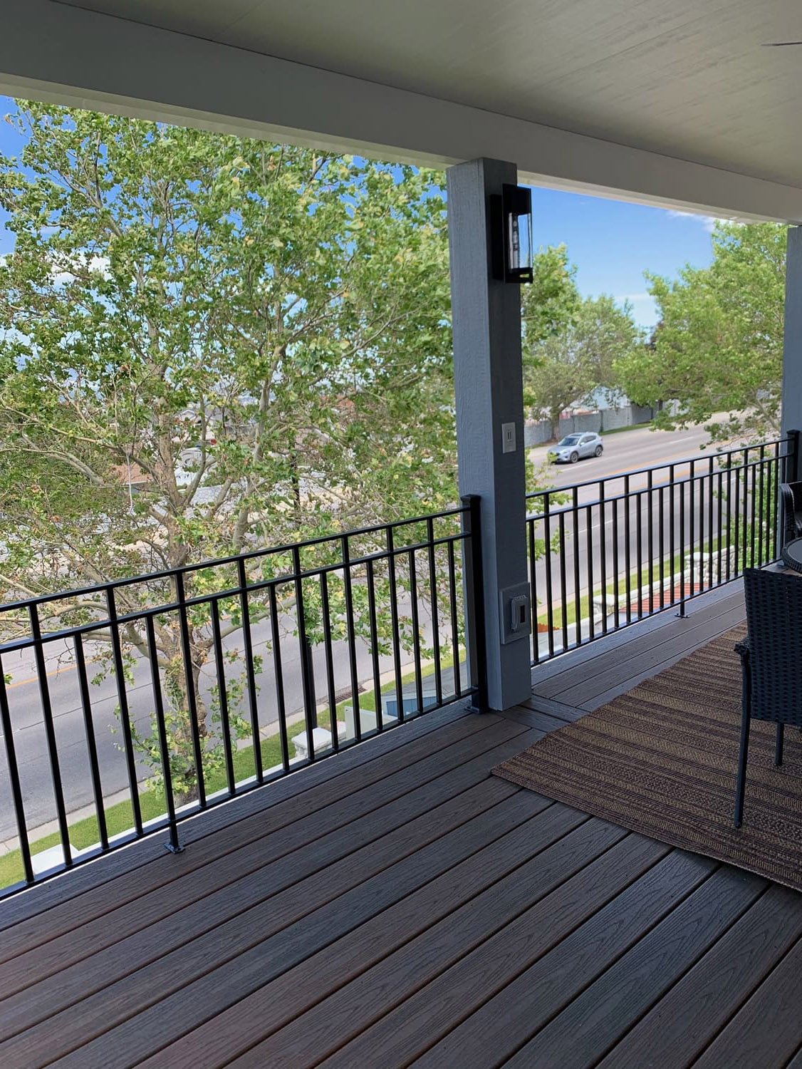 Trex-Transcend-Spiced-Rum-14 A wooden deck with a metal railing overlooking a lush green wooded area on a sunny day.