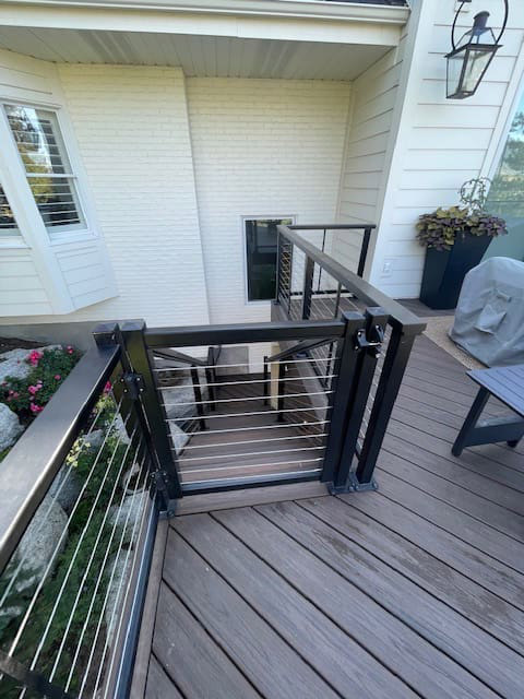 A close-up view of a wooden deck with a metal railing system, featuring a potted plant and other outdoor furniture