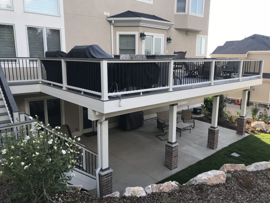 picture of a home with a second-story composite deck that has outdoor furniture and grills on it. a composite and aluminum railing surround the deck.