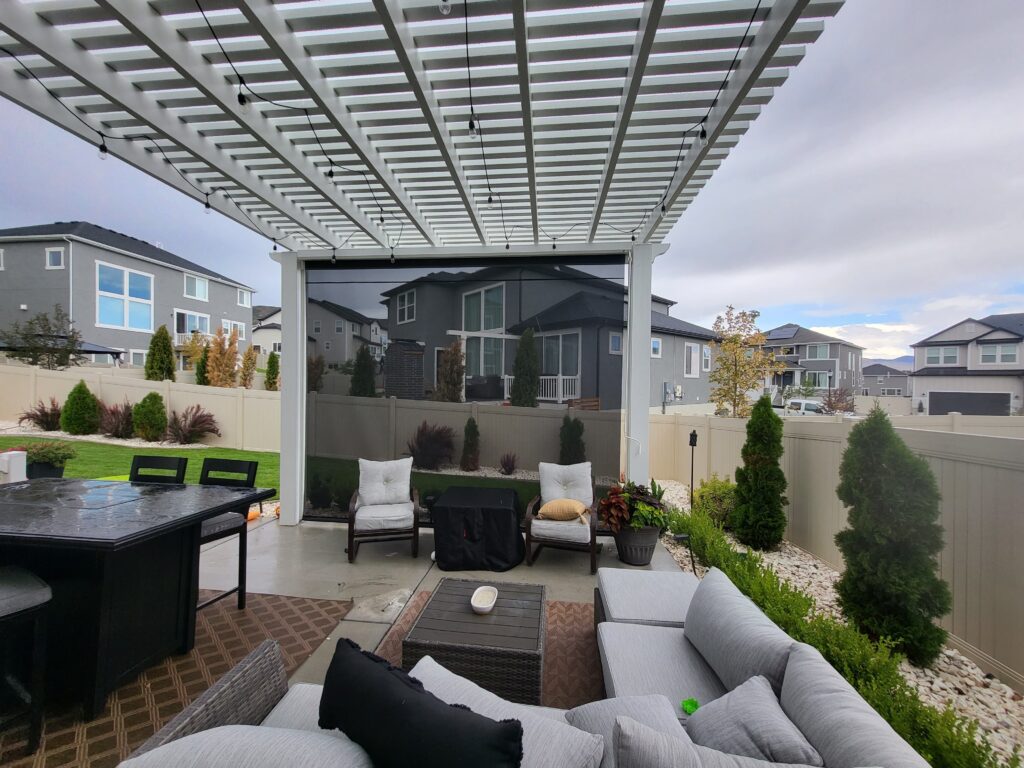 backyard patio space with a white pergola and a drop down sun shade.
